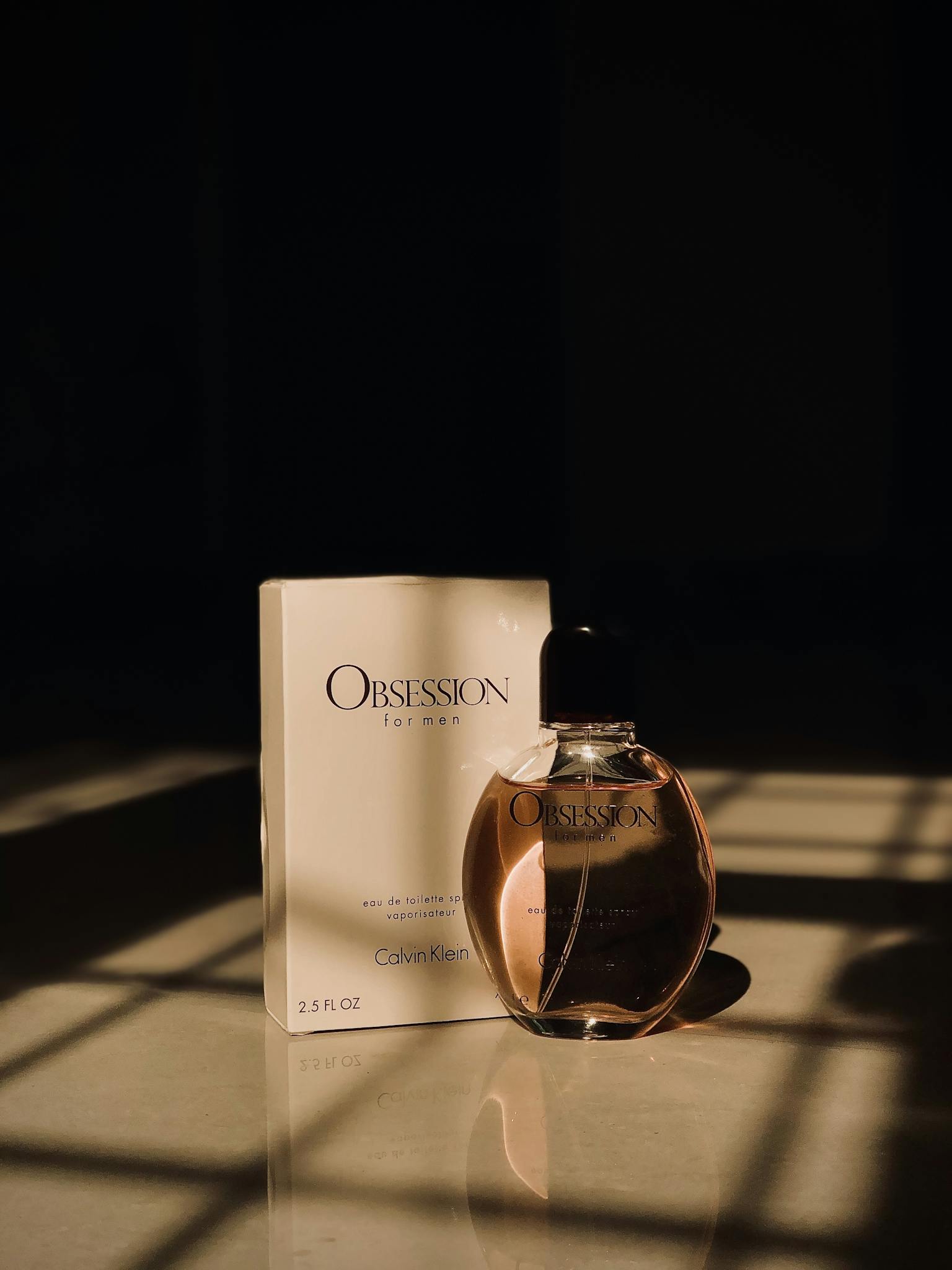 Calvin Klein Obsession perfume bottle beside its box captured in dramatic lighting.