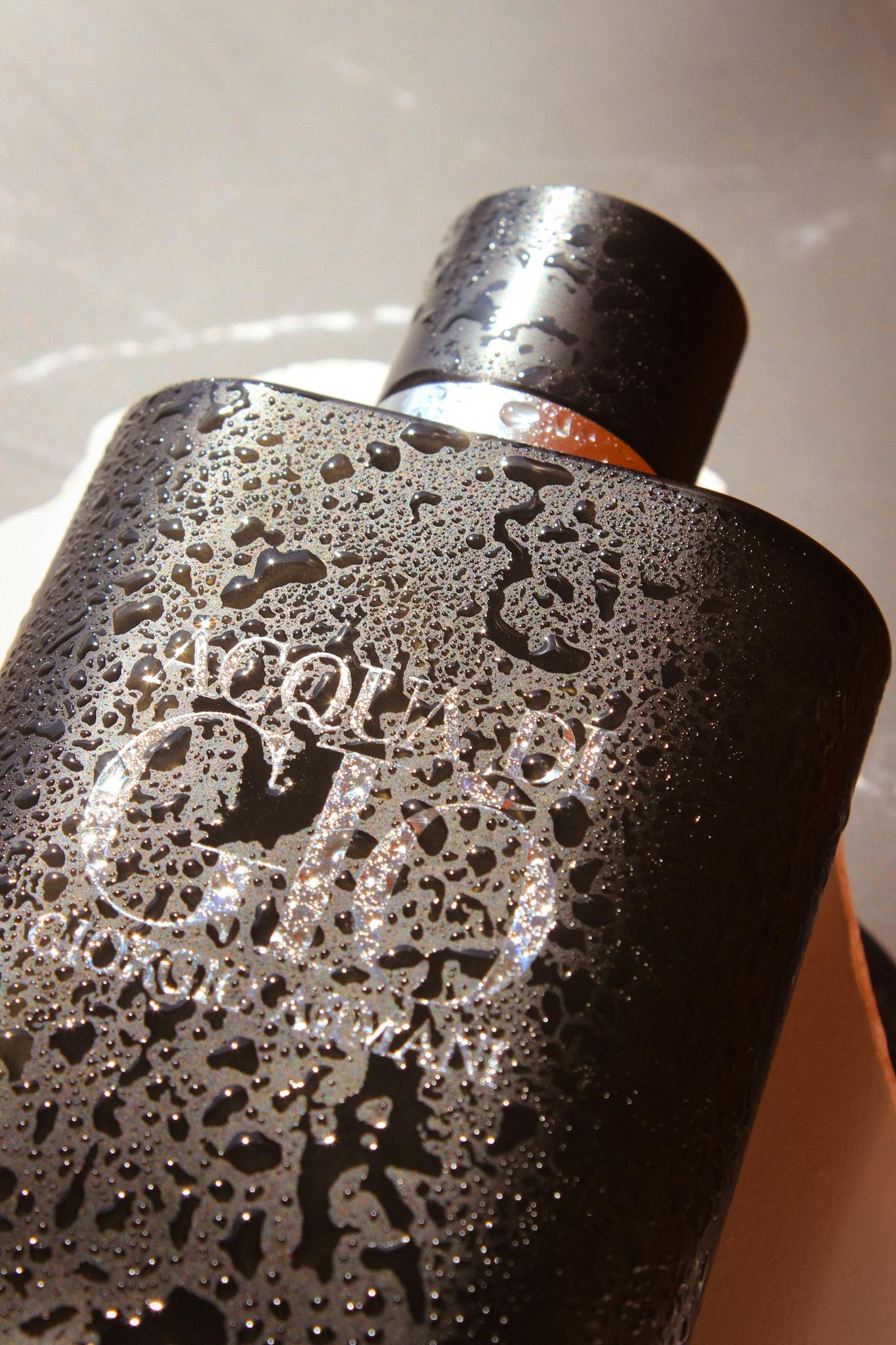Close-up of a sleek black perfume bottle covered with refreshing water droplets.