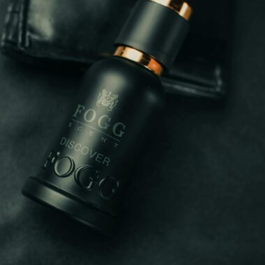 Close-up of a Fogg perfume bottle on a black surface with a leather wallet.